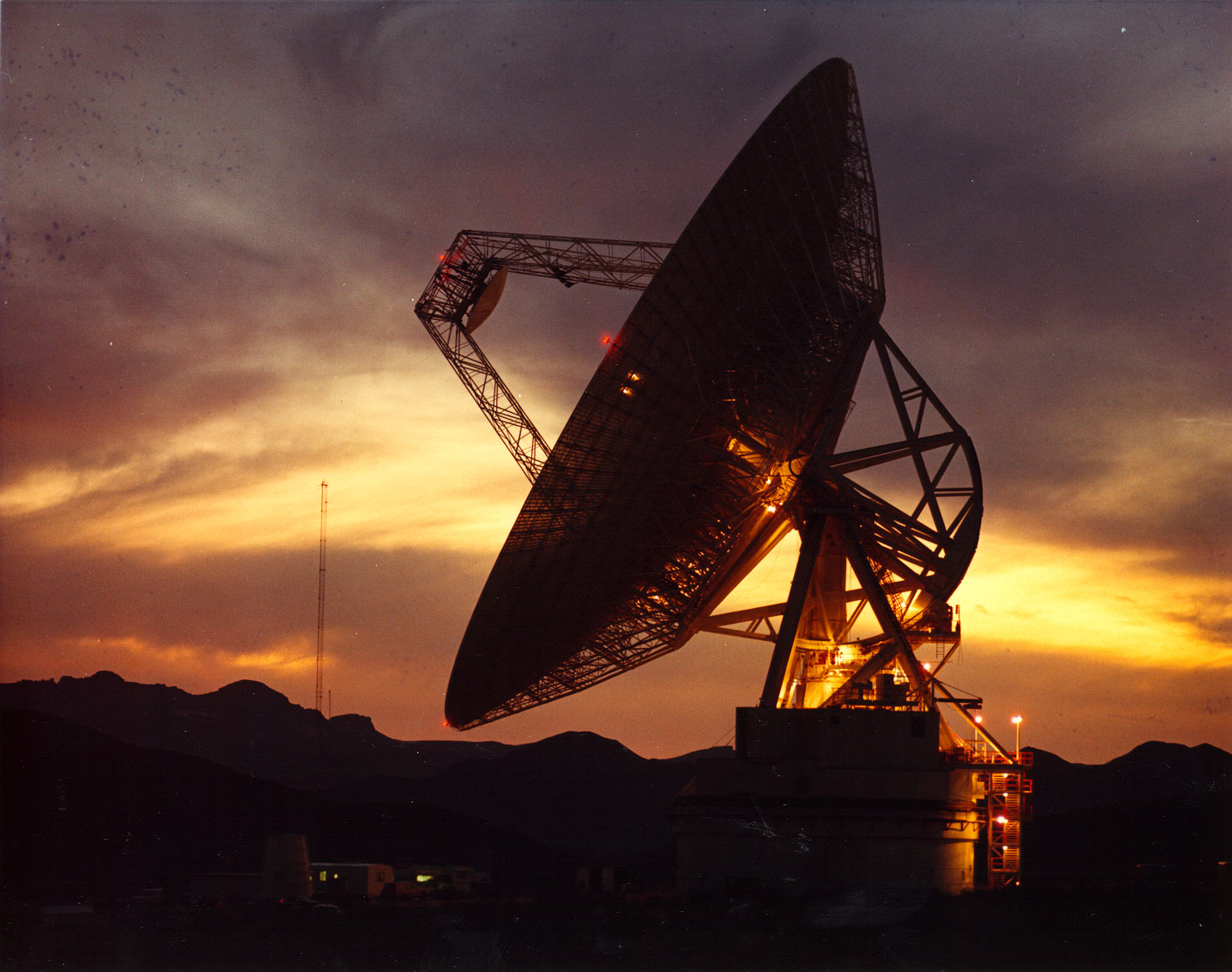 NASA Deep Space Network tracking antenna at sunset with a dramatic desert backdrop.